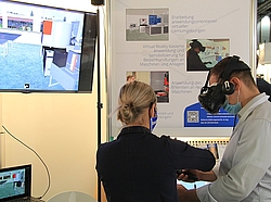 Wissenschaftlerin zeigt einem Besucher die Nutzung der VR-Brille