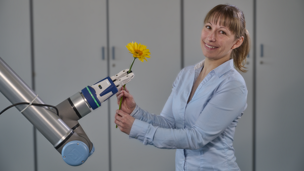 Roboterarm reicht Blume an weibliche Person