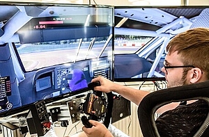 männliche Person sitzt vor gebogenem Monitor und fährt simulativ ein Autorennen