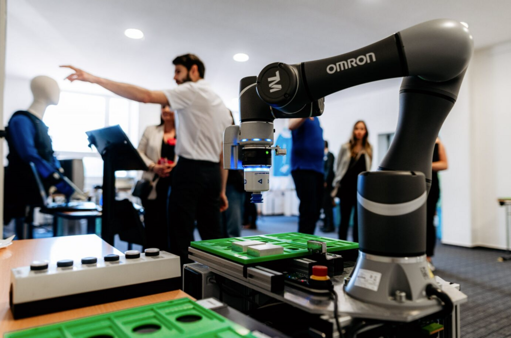 Ein Roboterarm steht im Vordergrund, im Hintergrund unterhalten sich Menschen