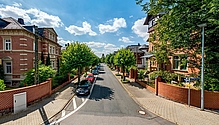 Bild der Poststraße mit Fahrzeugen, Häusern und Bäumen