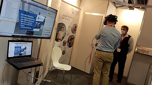 Herr Eckardt zeigt einem Besucher die VR Brille