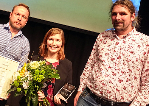 Preisträgerin Vicky Laura Eleser hält einen Blumenstrauß in der Hand, links an ihrer Seite steht Nico Müller von der Digifors GmbH, rechts Prof. Dr. Christian Hummert von der Hochschule Mittweida.