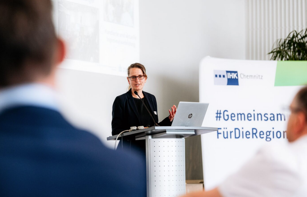 Professorin Julia Zähr steht am Pult und spricht zum Publikum