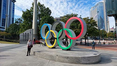 weibliche Person vor Hochhäusern und olympischem Logo
