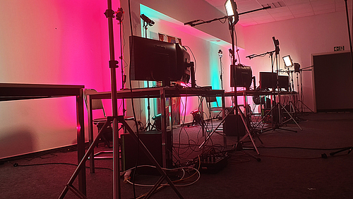 Blick in einen Raum, rosa beleuchtet, mit Scheinwerfern, Arbeitstischen und Rechnern