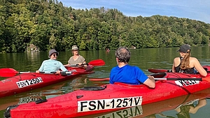 Zwei Kanus mit vier personen auf Wasser vor bewaldetem Ufer